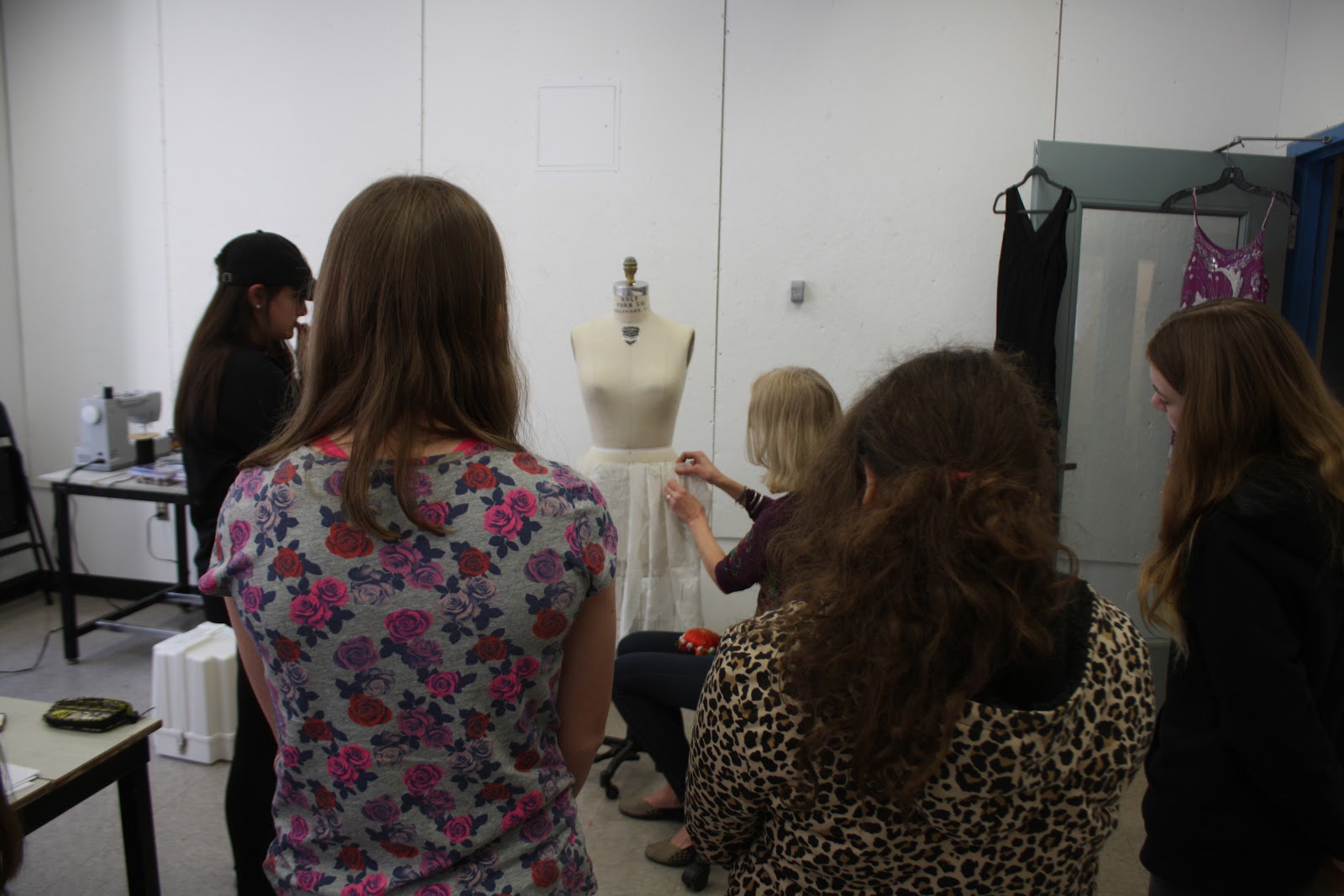 Teens gathered around a woman using a dressmaking model.